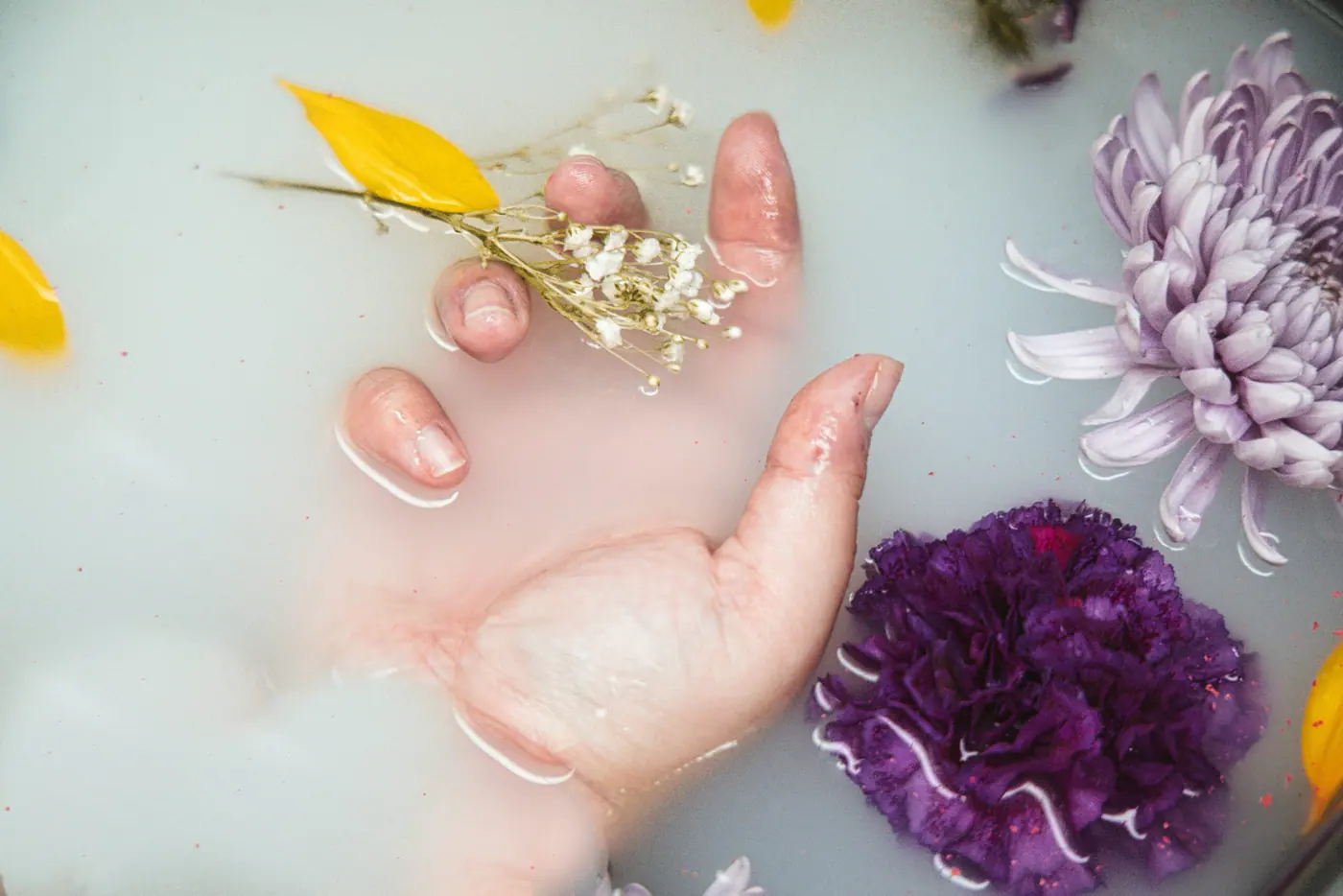 Đôi bàn tay đang được ngâm trong bát nước ấm với cánh hoa, giúp làm mềm da và thư giãn móng tay.